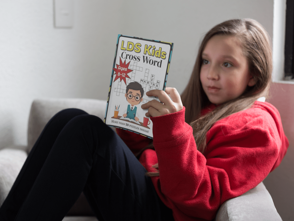 A girl aged 8-12 is reading and solving the LDS Kids Cross Word Book.